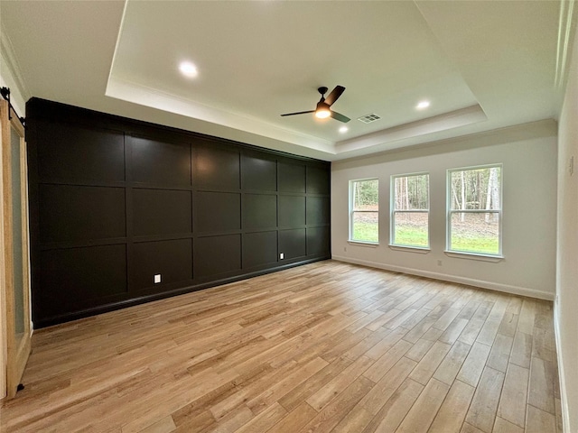 empty room with light hardwood / wood-style floors, a raised ceiling, ceiling fan, and a barn door