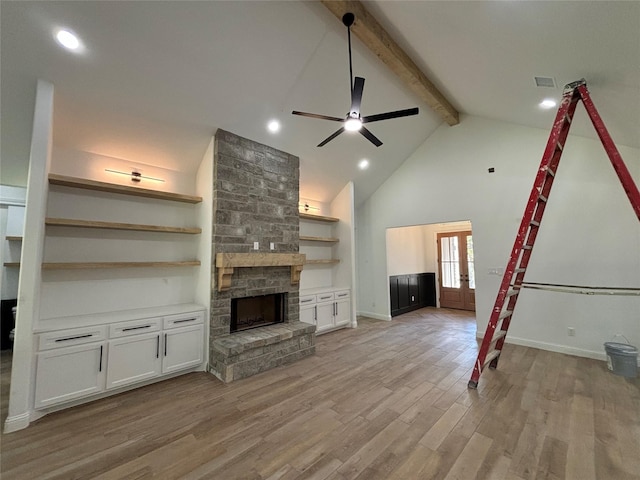 unfurnished living room with light hardwood / wood-style flooring, ceiling fan, high vaulted ceiling, a stone fireplace, and beamed ceiling