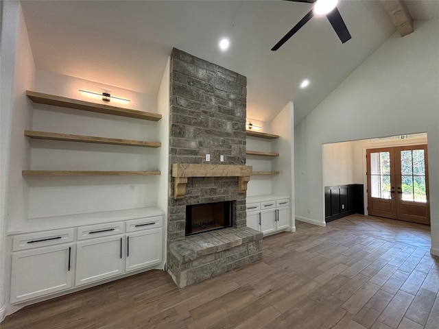 unfurnished living room featuring french doors, a stone fireplace, beamed ceiling, ceiling fan, and hardwood / wood-style floors