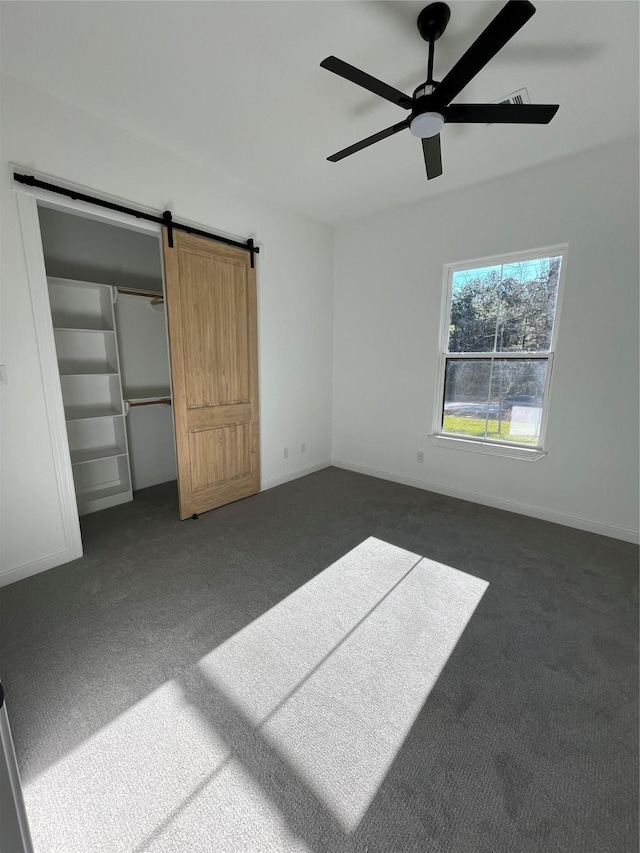 unfurnished bedroom featuring a closet, dark carpet, a barn door, and ceiling fan