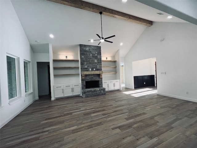 unfurnished living room featuring dark hardwood / wood-style flooring, beam ceiling, a stone fireplace, and ceiling fan