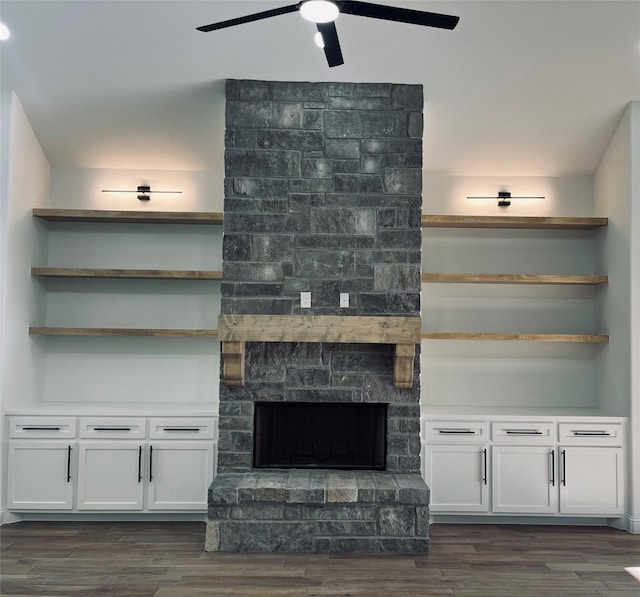 living room featuring dark wood-type flooring, ceiling fan, and a stone fireplace