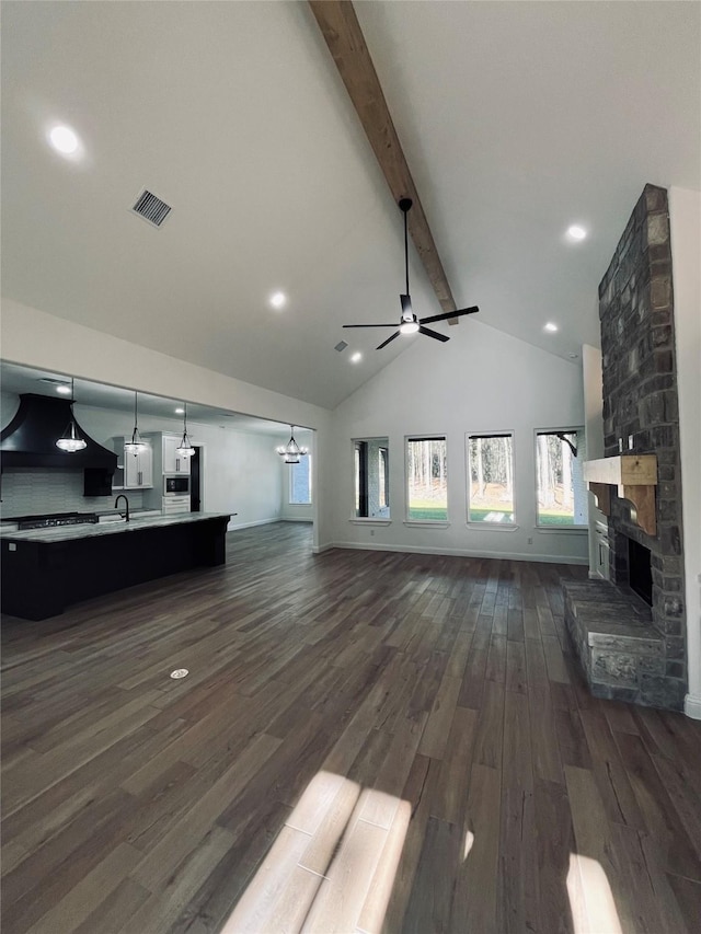 living room featuring sink, beam ceiling, plenty of natural light, dark hardwood / wood-style flooring, and a stone fireplace