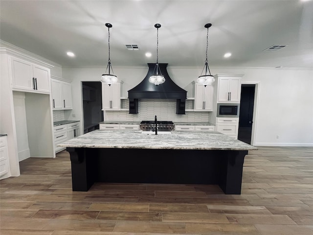 kitchen with a kitchen island with sink, black microwave, and premium range hood