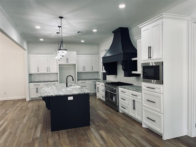 kitchen featuring built in microwave, white cabinetry, range with two ovens, a kitchen island with sink, and light stone countertops