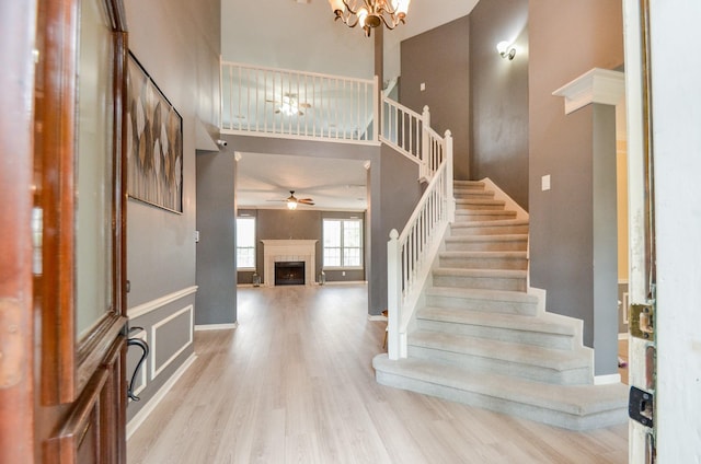 stairway featuring hardwood / wood-style flooring, ceiling fan with notable chandelier, a towering ceiling, and a tile fireplace