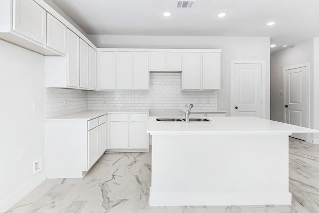 kitchen with backsplash, white cabinetry, sink, and an island with sink