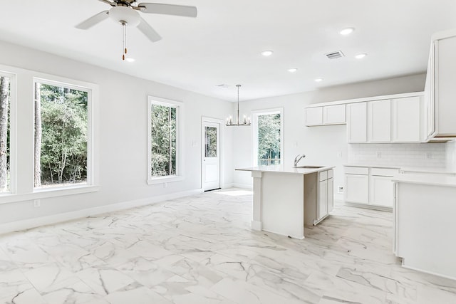 kitchen featuring white cabinetry, sink, tasteful backsplash, an island with sink, and pendant lighting