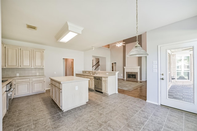 kitchen featuring backsplash, ceiling fan, a tile fireplace, decorative light fixtures, and a center island