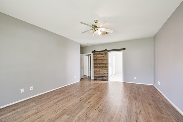 empty room featuring ceiling fan, a barn door, and light wood-type flooring