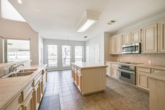 kitchen featuring tile countertops, a center island, sink, appliances with stainless steel finishes, and tasteful backsplash