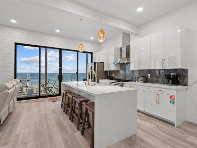 kitchen with wall chimney range hood, a water view, light hardwood / wood-style floors, white cabinetry, and hanging light fixtures