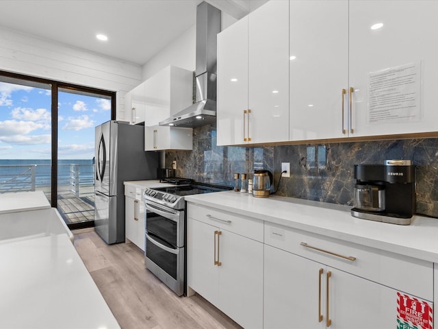 kitchen with white cabinetry, wall chimney exhaust hood, stainless steel appliances, light hardwood / wood-style floors, and a water view