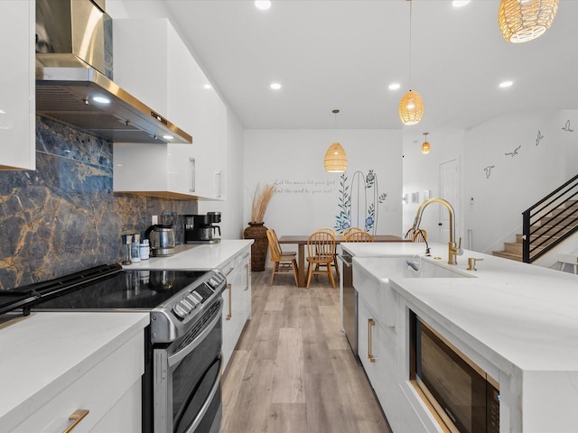 kitchen with hanging light fixtures, white cabinets, stainless steel appliances, and wall chimney range hood