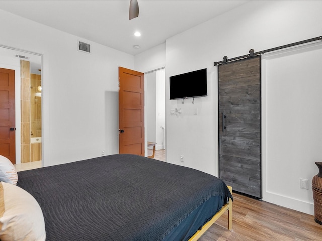 bedroom featuring ceiling fan, a barn door, light hardwood / wood-style flooring, and ensuite bath