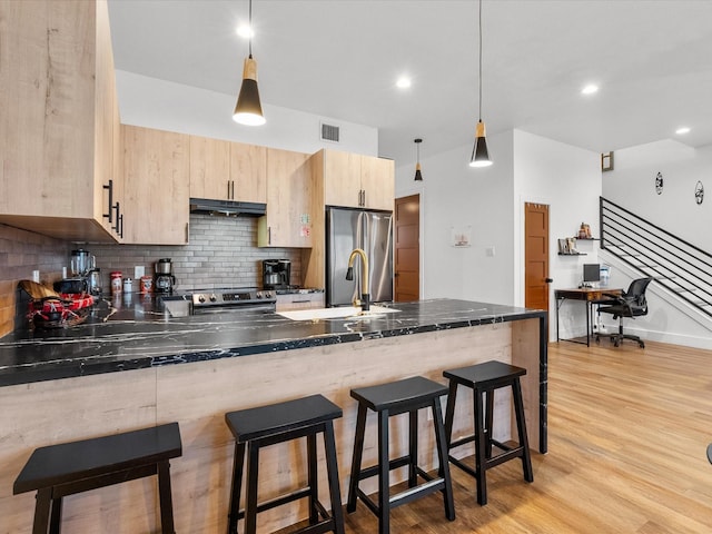 kitchen with kitchen peninsula, light brown cabinetry, appliances with stainless steel finishes, decorative light fixtures, and light hardwood / wood-style flooring