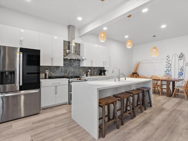 kitchen featuring white cabinetry, wall chimney exhaust hood, stainless steel appliances, light hardwood / wood-style floors, and decorative light fixtures