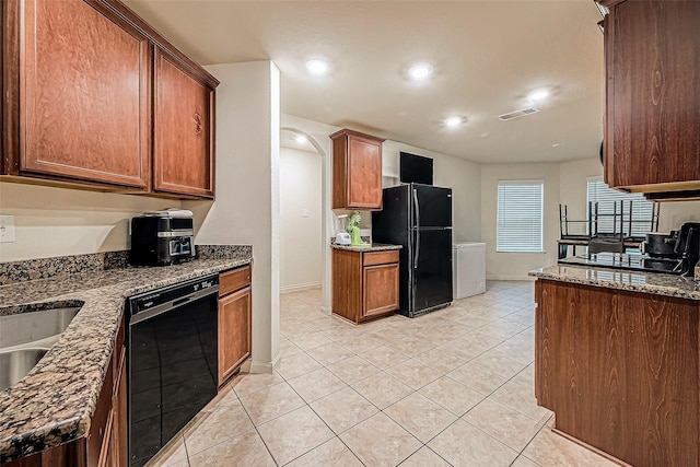 kitchen featuring dark stone countertops, sink, light tile patterned flooring, and black appliances