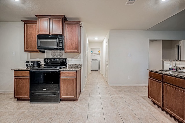 kitchen featuring dark stone countertops, sink, light tile patterned floors, and black appliances