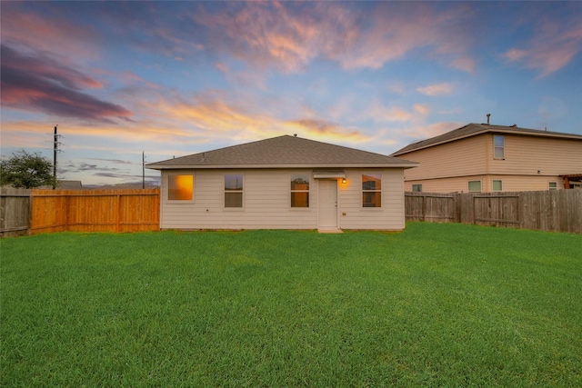 back house at dusk featuring a lawn