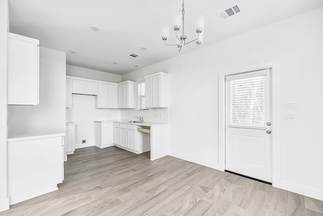 kitchen featuring sink, an inviting chandelier, light hardwood / wood-style flooring, backsplash, and white cabinets