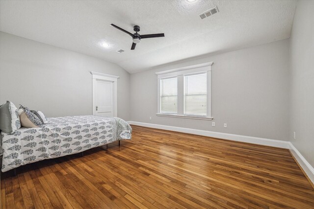 bedroom with wood-type flooring, a textured ceiling, vaulted ceiling, and ceiling fan