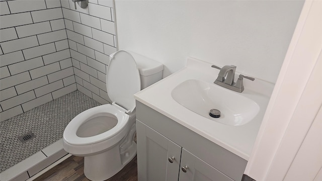 bathroom featuring hardwood / wood-style flooring, toilet, a tile shower, and vanity