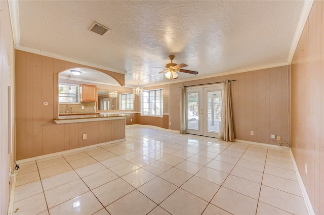 tiled spare room with a textured ceiling, crown molding, wood walls, and ceiling fan with notable chandelier