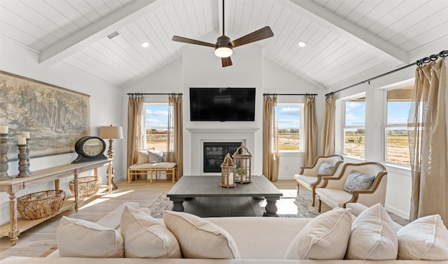 living room featuring vaulted ceiling with beams, a healthy amount of sunlight, light wood-style floors, and a glass covered fireplace