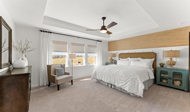 bedroom with ceiling fan, baseboards, a raised ceiling, and light colored carpet