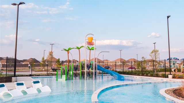 view of pool featuring a water slide, playground community, fence, a water play area, and a residential view