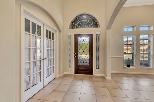 entrance foyer featuring light tile patterned floors, crown molding, a high ceiling, and french doors