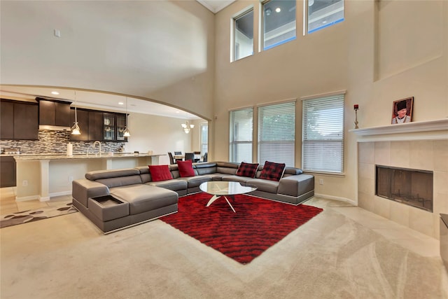 carpeted living room featuring a towering ceiling, a notable chandelier, a healthy amount of sunlight, and a tiled fireplace