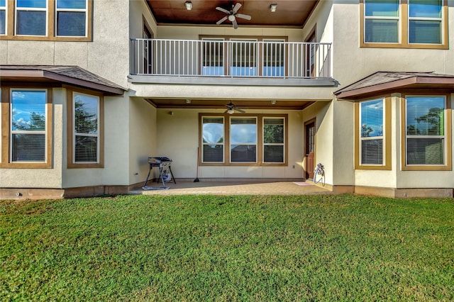 rear view of property featuring ceiling fan, a balcony, a yard, and a patio