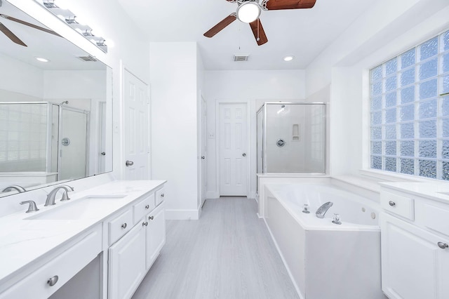 bathroom with plus walk in shower, hardwood / wood-style floors, vanity, and ceiling fan