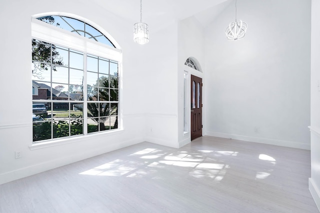 unfurnished room featuring light hardwood / wood-style floors, high vaulted ceiling, and a chandelier