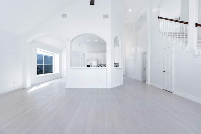 unfurnished living room featuring ceiling fan, light wood-type flooring, and high vaulted ceiling