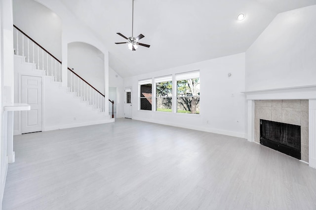 unfurnished living room featuring a tiled fireplace, ceiling fan, high vaulted ceiling, and light hardwood / wood-style floors