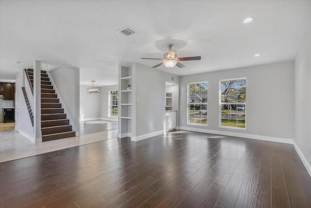 unfurnished living room featuring ceiling fan with notable chandelier and dark hardwood / wood-style floors