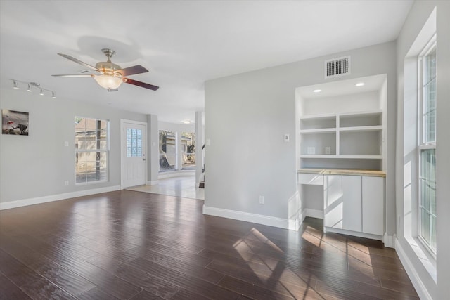 unfurnished living room with built in shelves, ceiling fan, and dark wood-type flooring