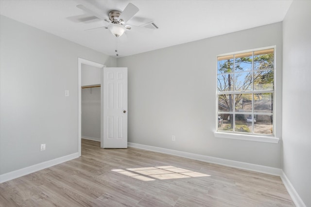 unfurnished bedroom featuring ceiling fan, a closet, a spacious closet, and light wood-type flooring