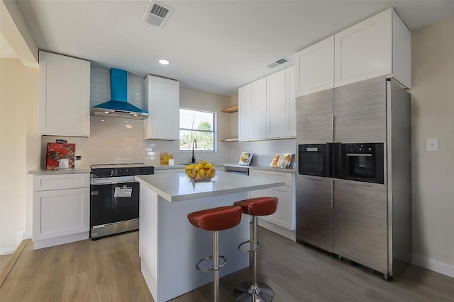 kitchen with white cabinets, stainless steel appliances, light hardwood / wood-style flooring, and wall chimney exhaust hood