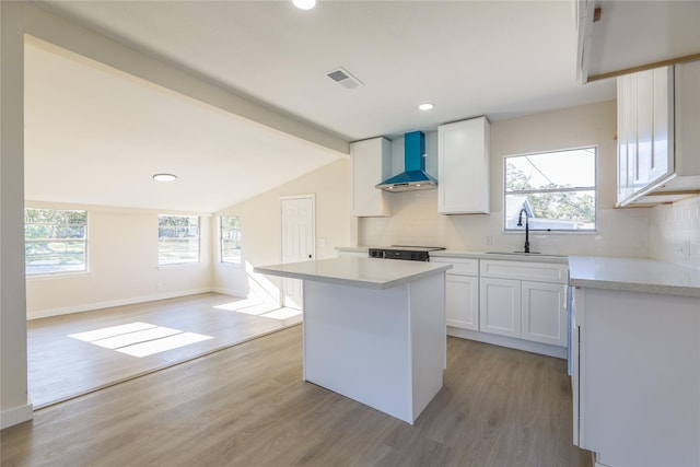 kitchen featuring white cabinets, sink, a kitchen island, and wall chimney range hood