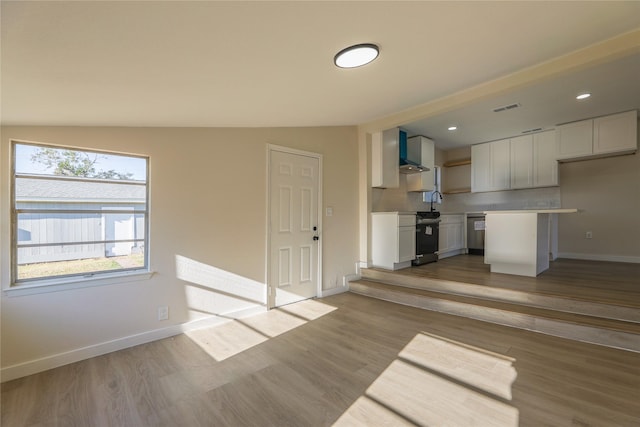 kitchen featuring backsplash, vaulted ceiling, wall chimney range hood, white cabinets, and light hardwood / wood-style floors