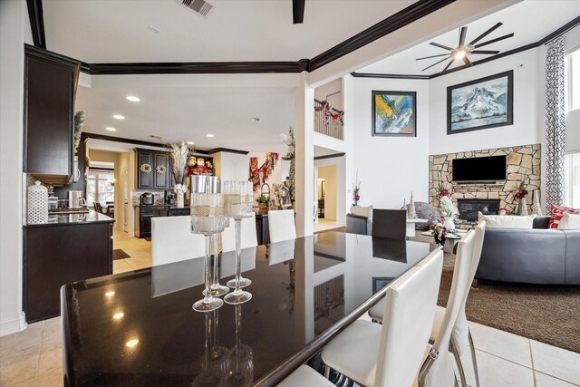 tiled dining area with ceiling fan, crown molding, and a fireplace