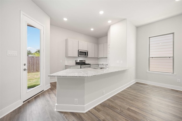 kitchen featuring light stone counters, white cabinetry, stainless steel appliances, and light hardwood / wood-style flooring