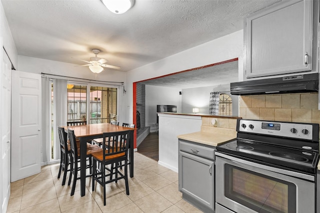 kitchen with stainless steel electric range oven, ceiling fan, backsplash, a textured ceiling, and light tile patterned flooring