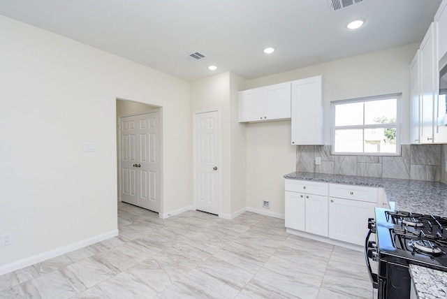 kitchen with backsplash, white cabinetry, stainless steel gas stove, and light stone counters