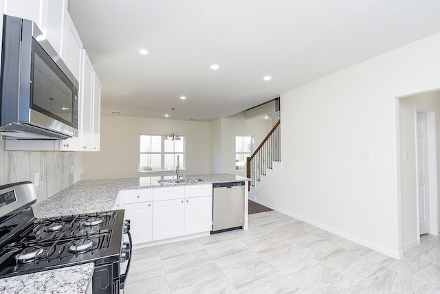 kitchen featuring kitchen peninsula, appliances with stainless steel finishes, light stone counters, sink, and white cabinets