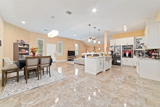 kitchen with white cabinetry, ceiling fan, backsplash, an island with sink, and decorative light fixtures